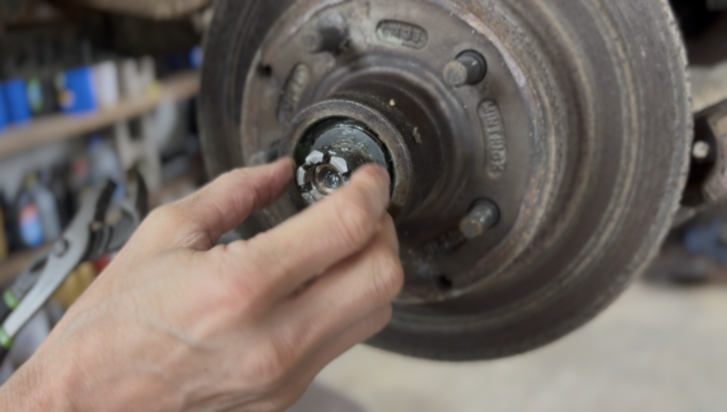 bearing A close-up of a person's hands working on a car's wheel bearing and brake assembly.
